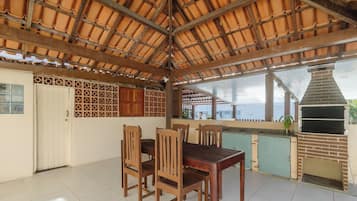 Uma área de refeições ao ar livre coberta, com forno a lenha, cadeiras de madeira e piso de azulejos.