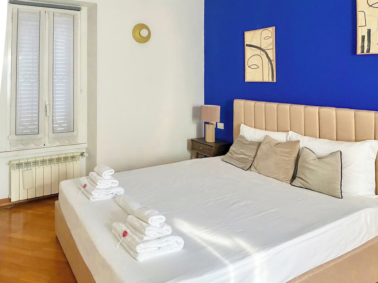 Ein Hotelzimmer mit Bett, Nachttisch, Lampe und Fenster mit Jalousien.