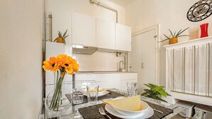 Una cocina moderna con armarios blancos, una campana extractora de acero inoxidable, una mesa de comedor de vidrio con posavasos y un reloj en la pared.