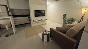Ein modernes Wohnzimmer mit einer Couch, einem Fernseher, einem Essbereich mit Tisch und Stühlen sowie einer Küche im Hintergrund.