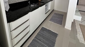 Eine moderne Küche mit weißen Schränken, einer schwarzen Arbeitsplatte und einer gefliesten Spritzschutzwand. Holzkocher hängen an der Wand und ein schwarz-weiß gestreifter Teppich liegt auf dem Boden.