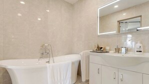 Et moderne badeværelse med et fristående badekar, et toiletbord med et spejl, og et stort spejl over vasken.