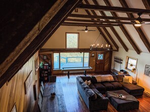 A loft-style room with a wooden ceiling, a large window, a dark-colored sofa, and a dining table.