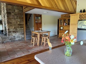 A rustic kitchen with a stone wall, wooden dining table, and a refrigerator. - A-Frame near PSU, Sleeps 10 + Sauna (Petersburg)