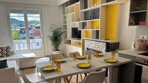 A modern kitchen with a dining area, featuring a large island, white cabinets, and a view through the window.