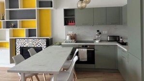 A modern kitchen with grey cabinets, a white countertop, and a dining area with a grey table and chairs.