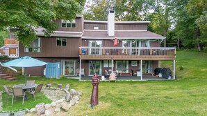 A two-story house with a balcony, a patio with outdoor furniture, and a sculpture in the yard.