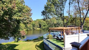A deck with a pergola and chairs overlooking a lake, surrounded by trees.