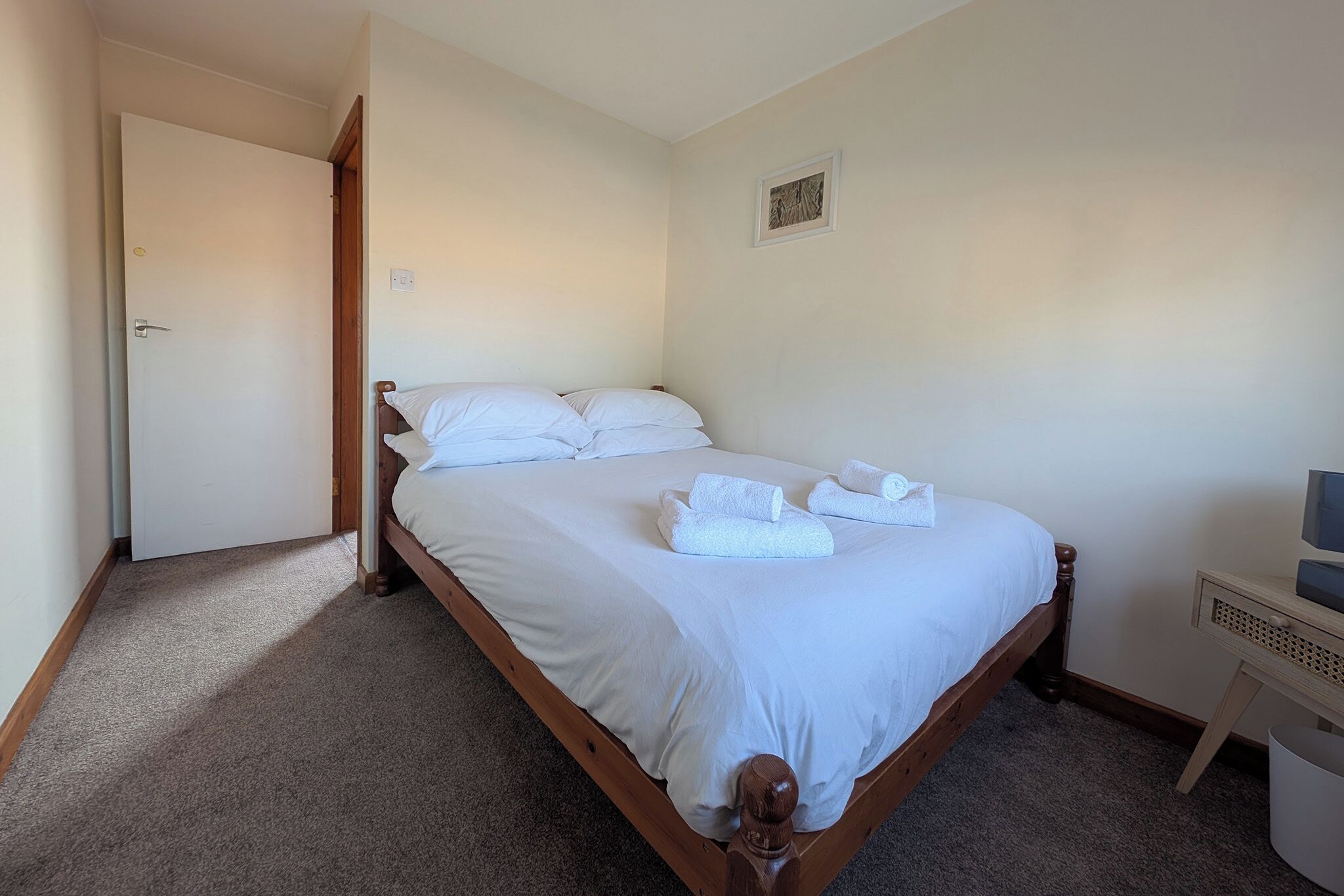 A neatly made bed with white linens and towels, a wooden headboard, and a small bedside table with a lamp.