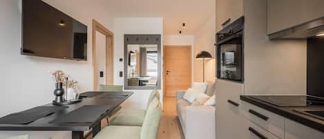 A modern kitchen with a built-in oven, a dining area with a table and chairs, and a living area with a sofa and a TV.
