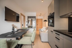 A modern kitchen with a built-in oven, a dining area with a table and chairs, and a living area with a sofa and a TV. - Apartment Near Schaterzlift Kirchberg (Kirchberg in Tirol)