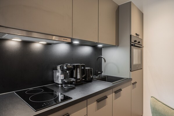 A modern kitchen with a black countertop, a built-in stove, a coffee maker, and a sink. - Apartment Near Schaterzlift Kirchberg (Kirchberg in Tirol)