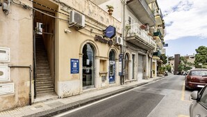 Straßenansicht eines Gebäudes mit dem Schriftzug 'Allianz', einschließlich Geldautomat, Treppe und geschlossenem Rolltor.