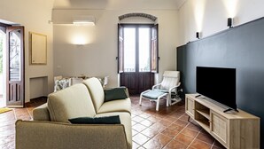 Ein Wohnzimmer mit einer Couch, Sesseln, einem Fernseher und einer Tür, die nach draußen führt.