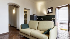 Ein Wohnzimmer mit einer Couch, einer Küchenzeile und einer Tür zu einem Außenbereich.