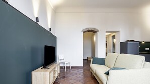 Ein modernes Wohnzimmer mit einem Flachbildfernseher, einem hellen Sofa, einem weißen Sessel und einem kleinen Holztisch.
