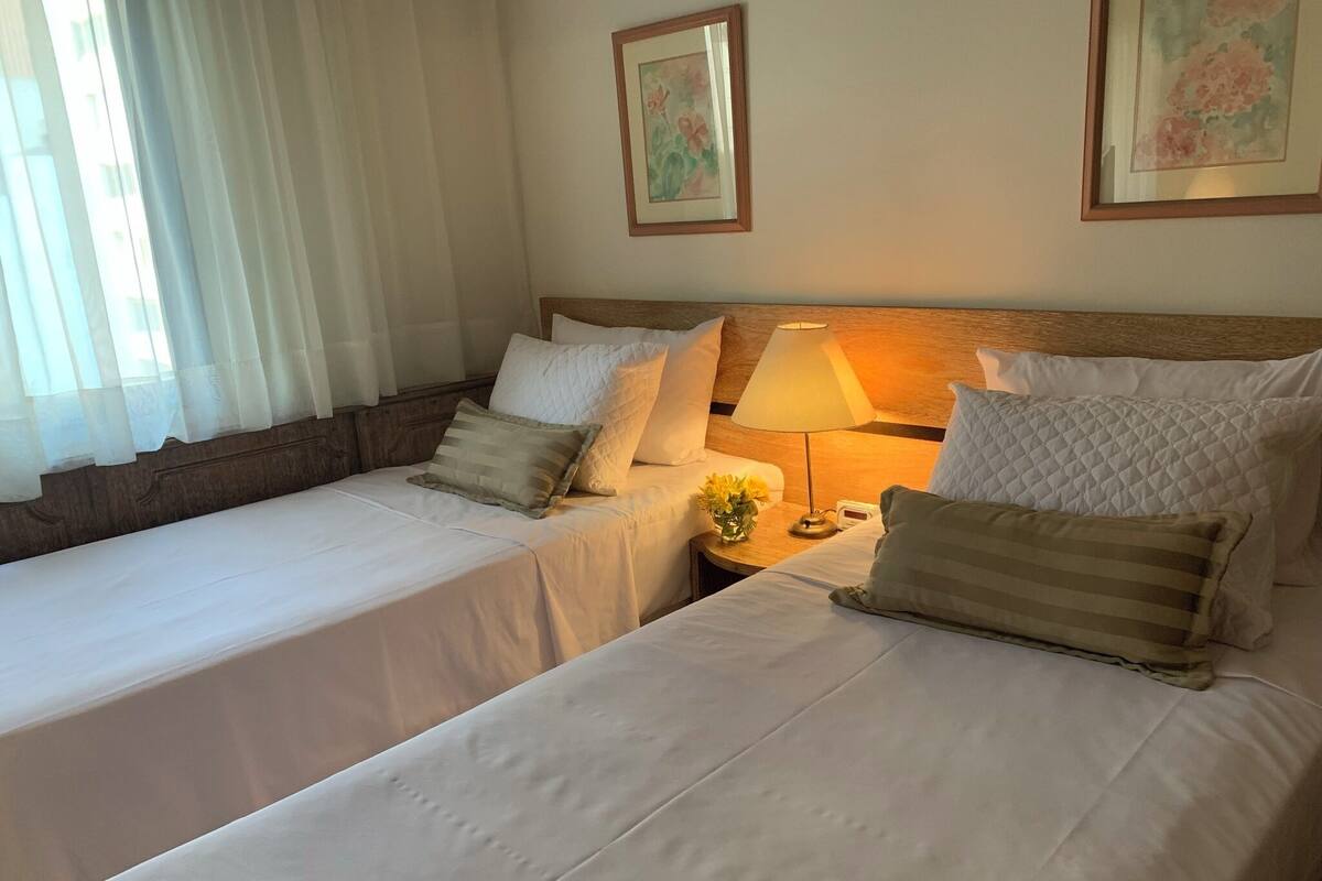 Una habitación de hotel con dos camas, una mesita de noche con lámpara y un jarrón con flores.
