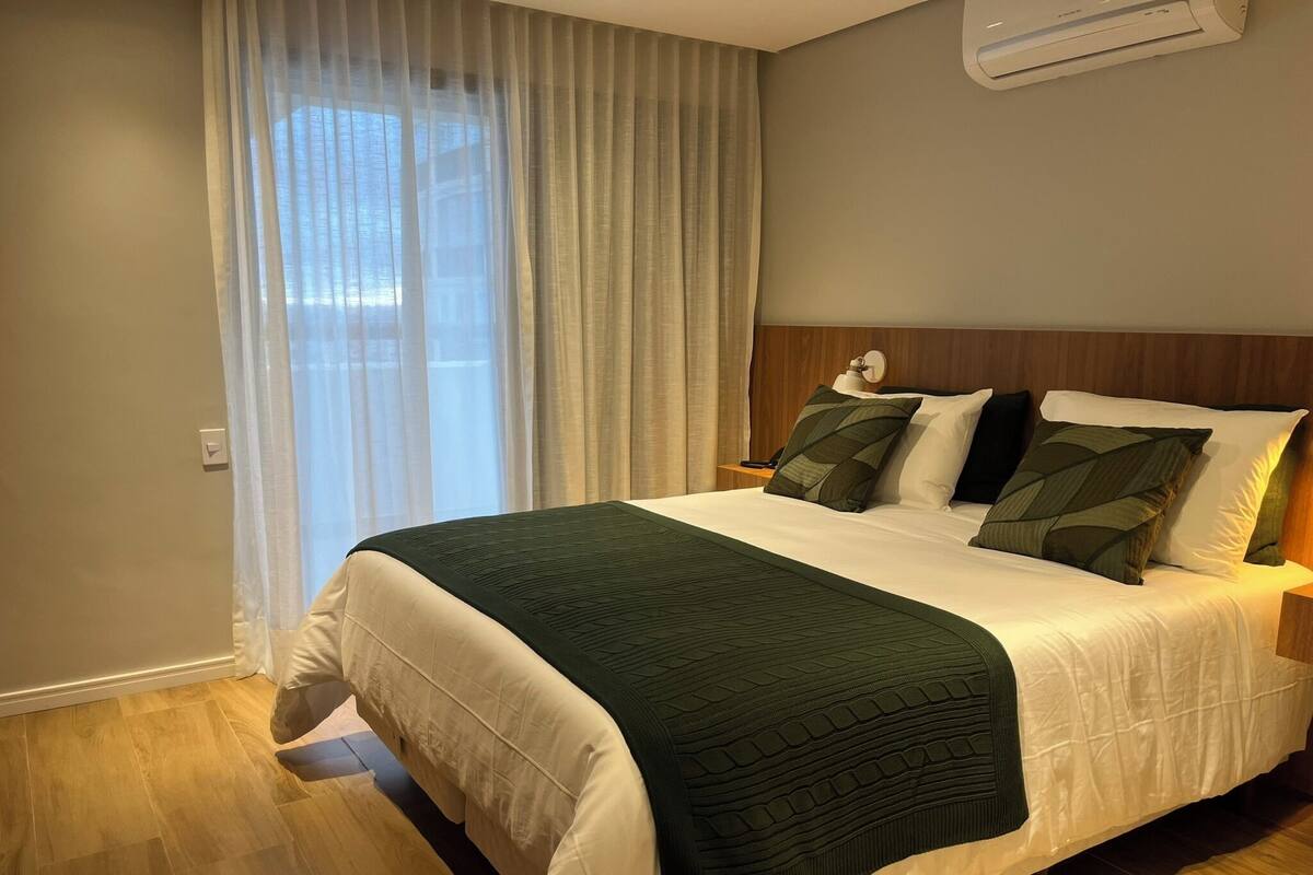 Una habitación de hotel con una cama, una mesita de noche, una lámpara y un equipo de aire acondicionado.