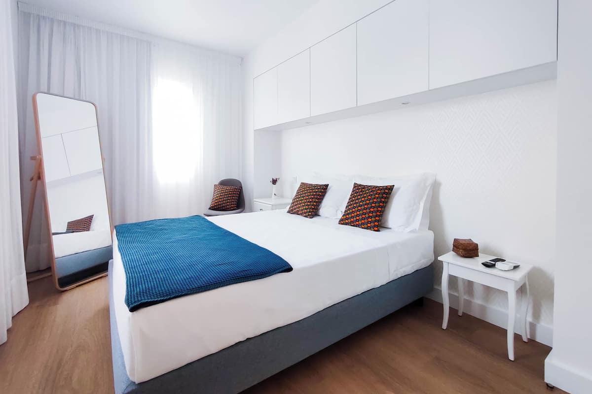Ein modernes Hotelzimmer mit einem großen Bett, einem Nachttisch, einem Spiegel und einem Fenster mit Vorhängen.