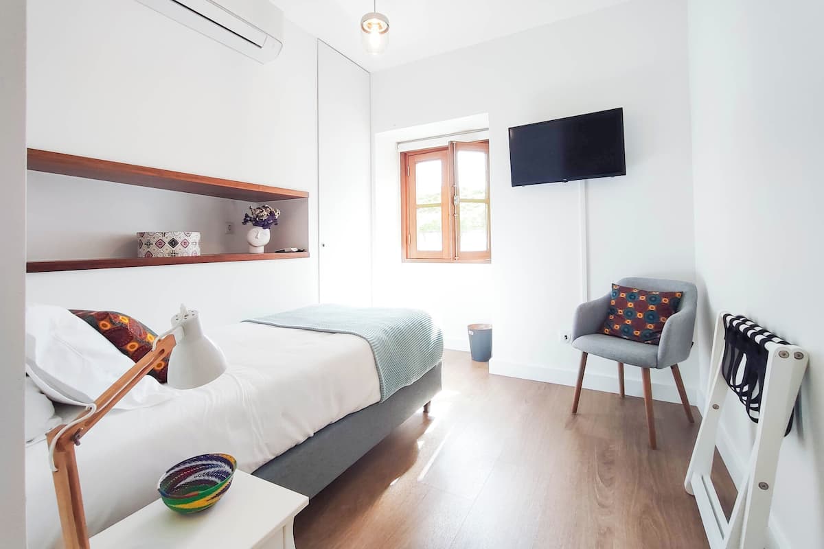 Ein modernes Schlafzimmer mit Bett, Sessel, Fernseher und Fenster.
