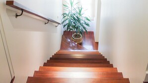 Una escalera de madera con barandilla, una planta en maceta en la parte superior y una lámpara en el techo.