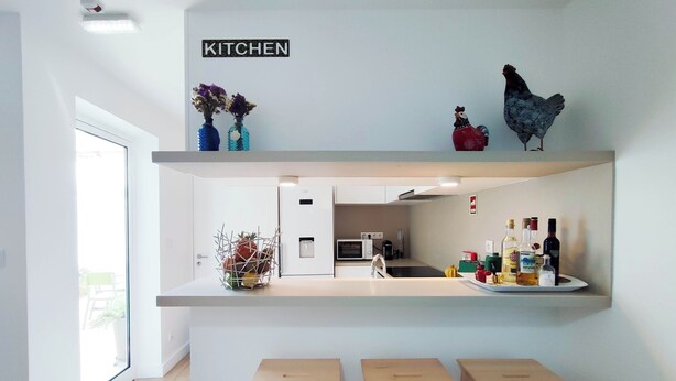 Una cocina moderna con un cartel que dice 'KITCHEN', un microondas, un fregadero y una encimera con botellas y un pollo decorativo.