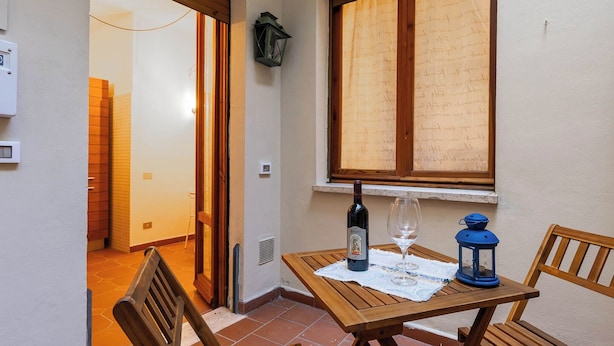 A small wooden table with a bottle and wine glass, a lantern, and a chair in a corner with a window.