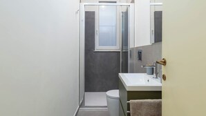 A narrow bathroom with a toilet, a sink, and a mirror.