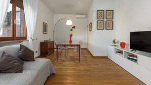 A compact living space with a sofa, a dining table with chairs, a TV, and artwork on the walls.