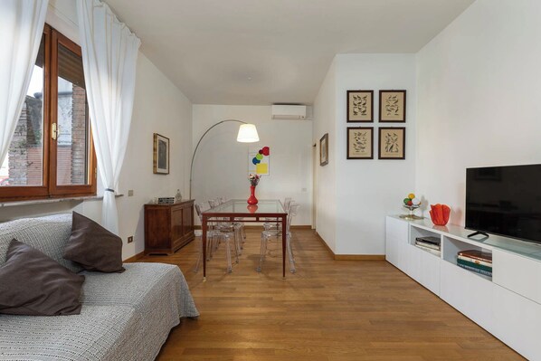 A compact living space with a sofa, a dining table with chairs, a TV, and artwork on the walls. - Elegant apartment in the setting of Siena with air conditioning, WI-FI and TV (Siena)
