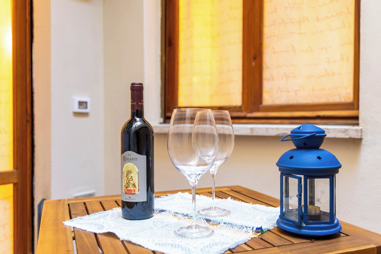 Une bouteille de vin, trois verres à vin et une lanterne bleue sur une table en bois.