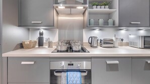 A modern kitchen with grey cabinets, a built-in oven, a microwave, and a kettle. - 1 Bed Flat - Sleeps 3 - Parking (Birmingham)