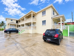 A two-story building with a balcony, a staircase, and a car parked in front. - Cassywins Short Term Rentals Apt #3 (Bridgetown)