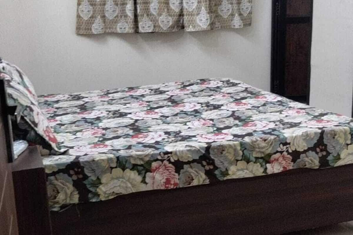 A bedroom with a bed, a window with patterned curtains, a door, and an air conditioning unit.
