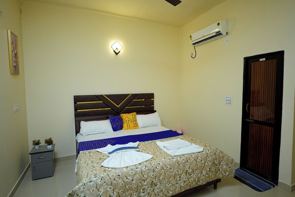 Habitación de hotel ordenada con cama, mesita de noche y unidad de aire acondicionado.
