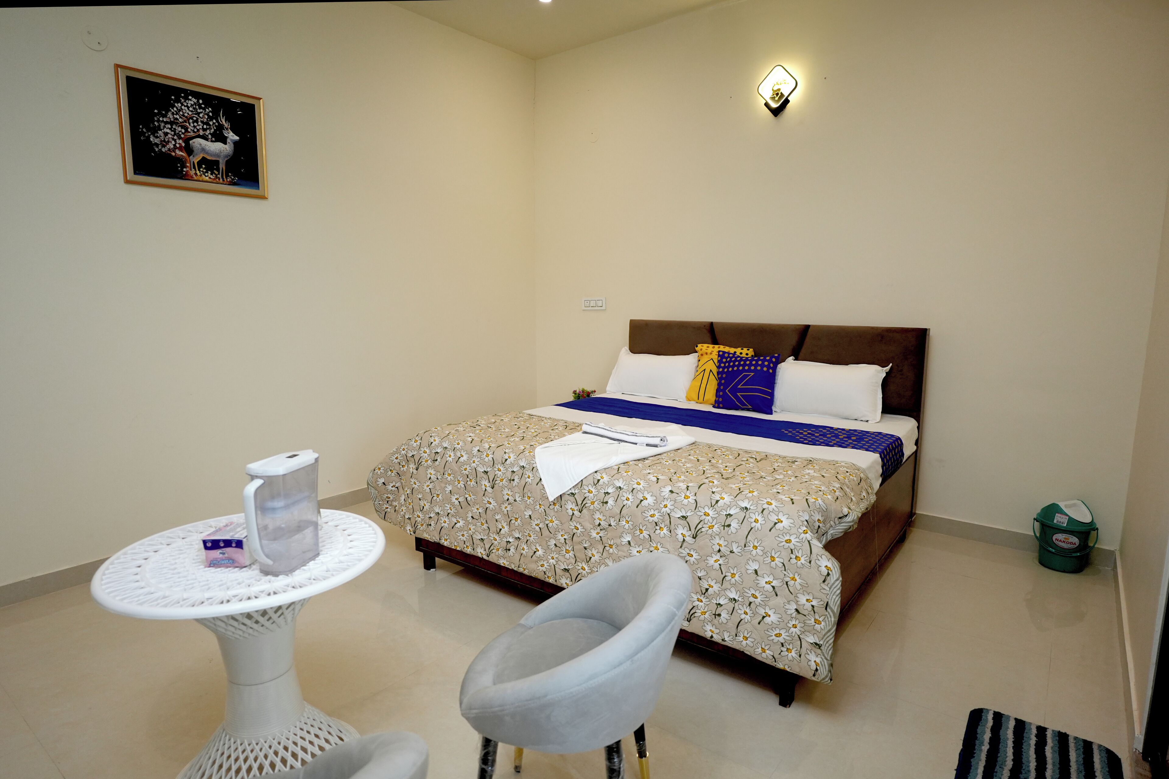 A bedroom with a bed, a chair, a small table, and a wall-mounted light fixture.