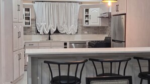 A modern kitchen with white cabinetry, a central island with bar stools, pendant lighting, and a backsplash with a stone pattern. - 3 min from Ogle Intl Airport 
Vacation Home in Prime Location (Ogle)