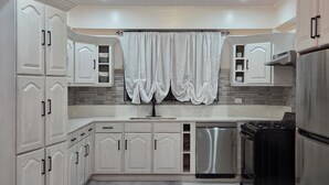 A modern kitchen with white cabinetry, a stainless steel refrigerator, and a black stove. - 3 min from Ogle Intl Airport 
Vacation Home in Prime Location (Ogle)
