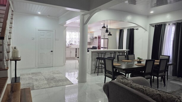 A spacious living area with a dining table, sofas, and a kitchen in the background. - 3 min from Ogle Intl Airport 
Vacation Home in Prime Location (Ogle)