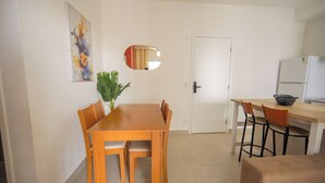 Ett kompakt bostadsutrymme med en matplats, ett litet kök och en dörr som leder till ett annat rum.