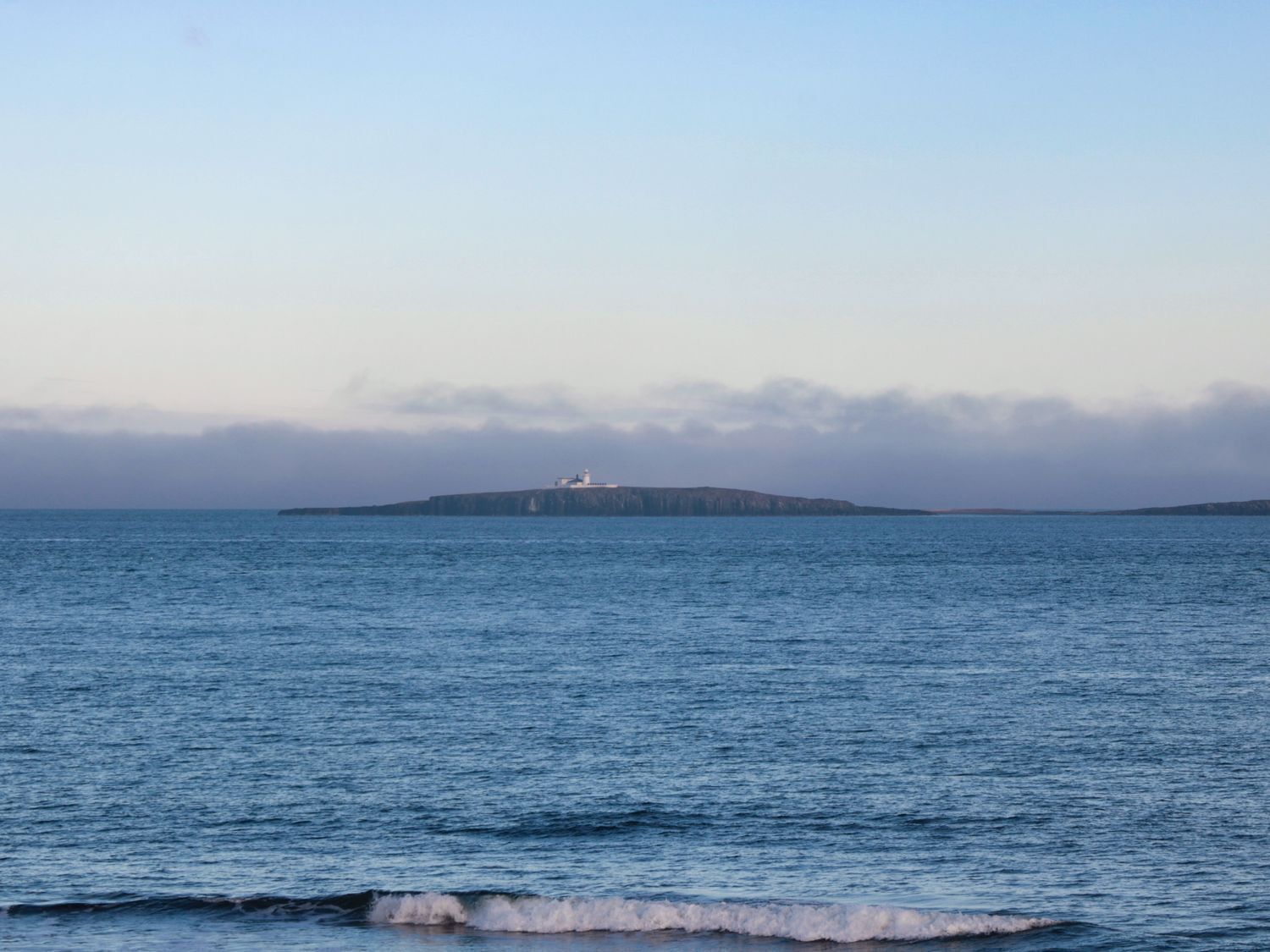 Un phare sur une petite île, avec une mer calme et un ciel nuageux.