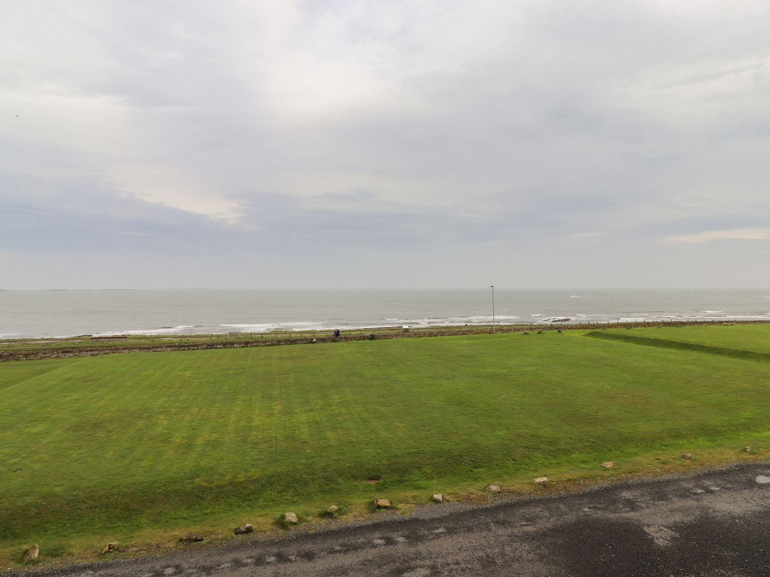 Vista costera con un campo verde y una carretera que lleva al mar.