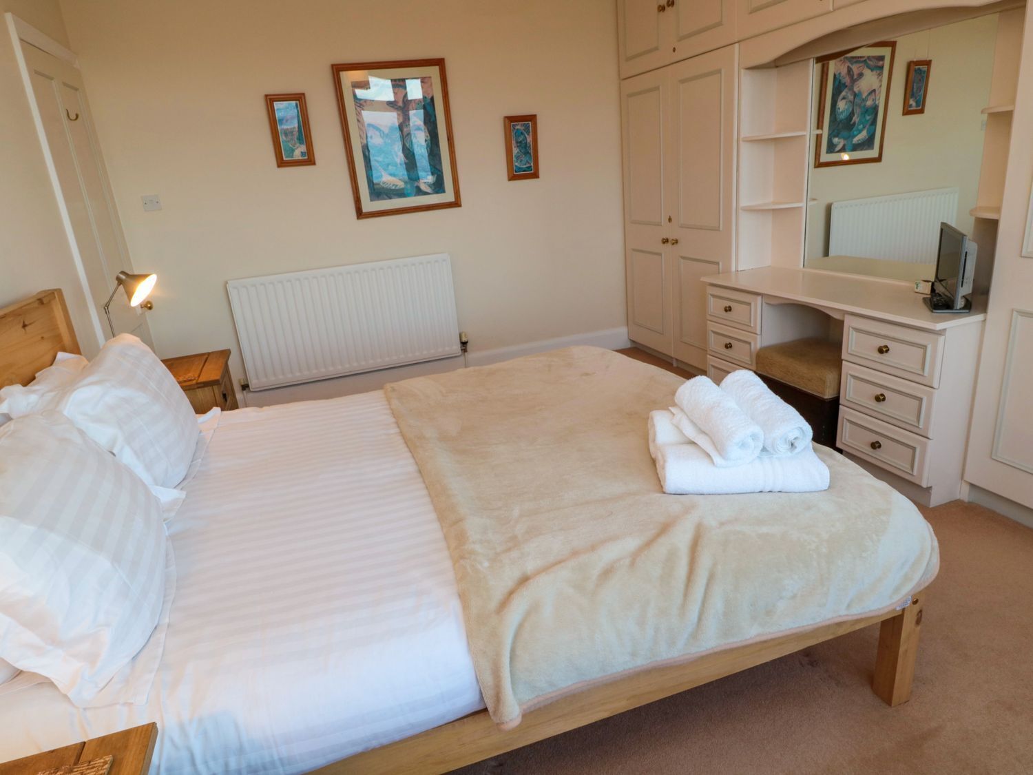 A bedroom with a bed, a nightstand, a dresser, a mirror, and wall art.