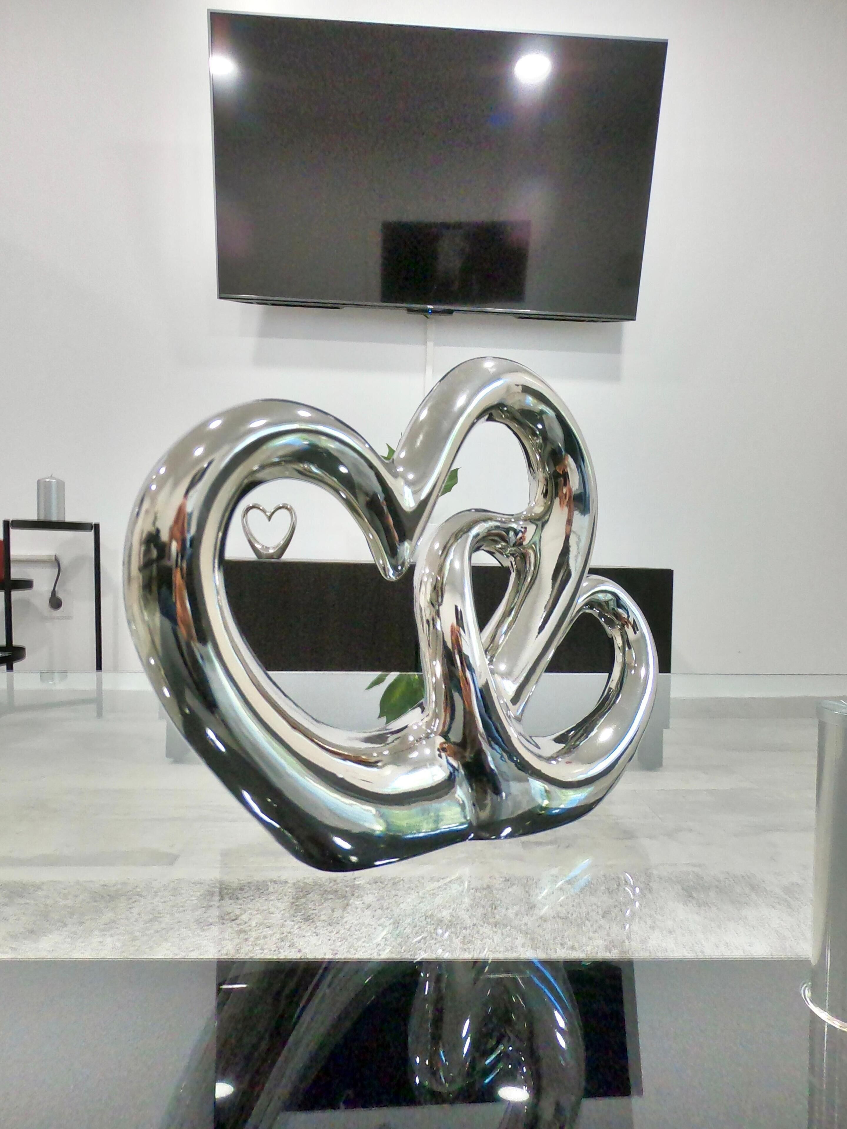 A heart-shaped sculpture on a reflective surface with a television mounted on the wall behind it.