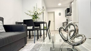 A modern living room with a sofa, a dining table with chairs, a decorative heart-shaped sculpture, and a kitchen area with cabinets and a microwave. - Naffah Apartments II (Madrid)