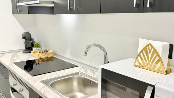 A modern kitchen with a built-in induction cooktop, a stainless steel sink, and a microwave. - Naffah Apartments II (Madrid)