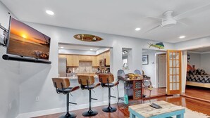 A modern living room with a bar area, wooden flooring, and a ceiling fan.