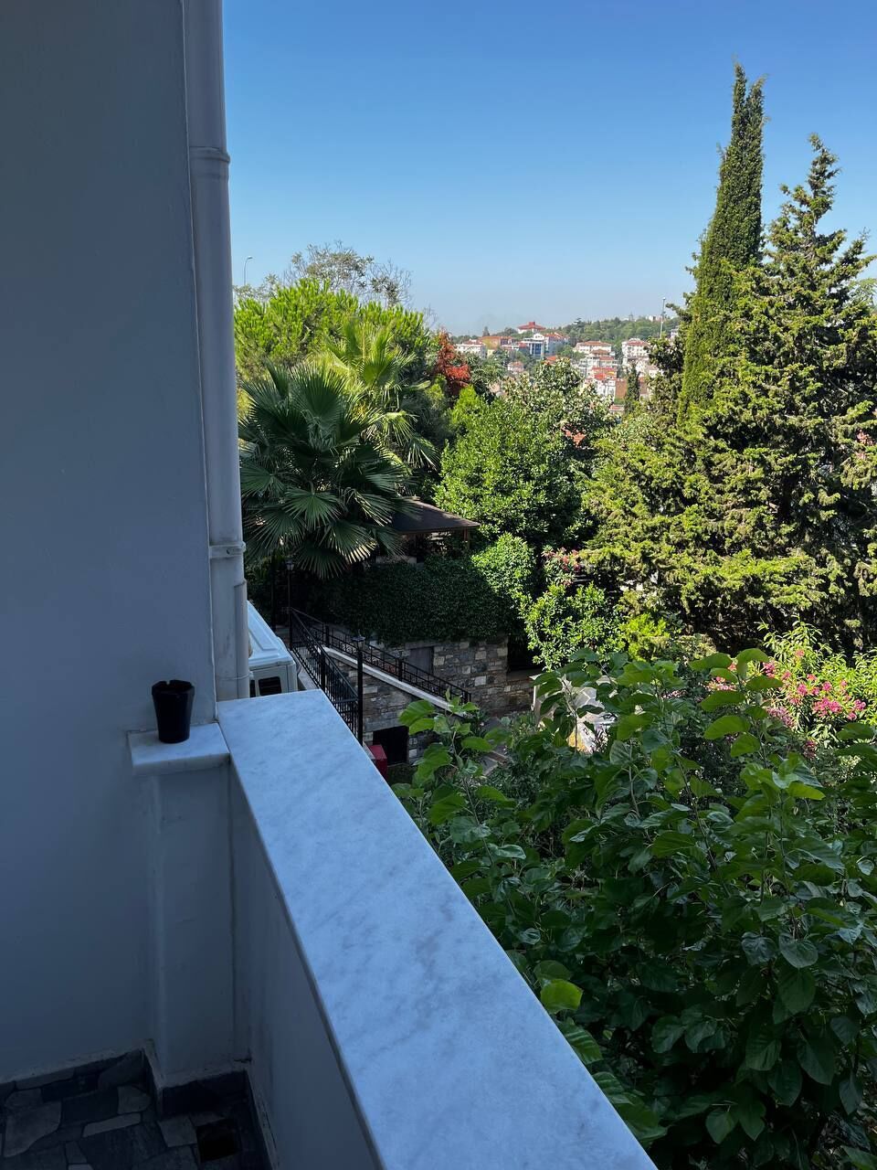 Un balcón con vista a un paisaje urbano y abundante vegetación.