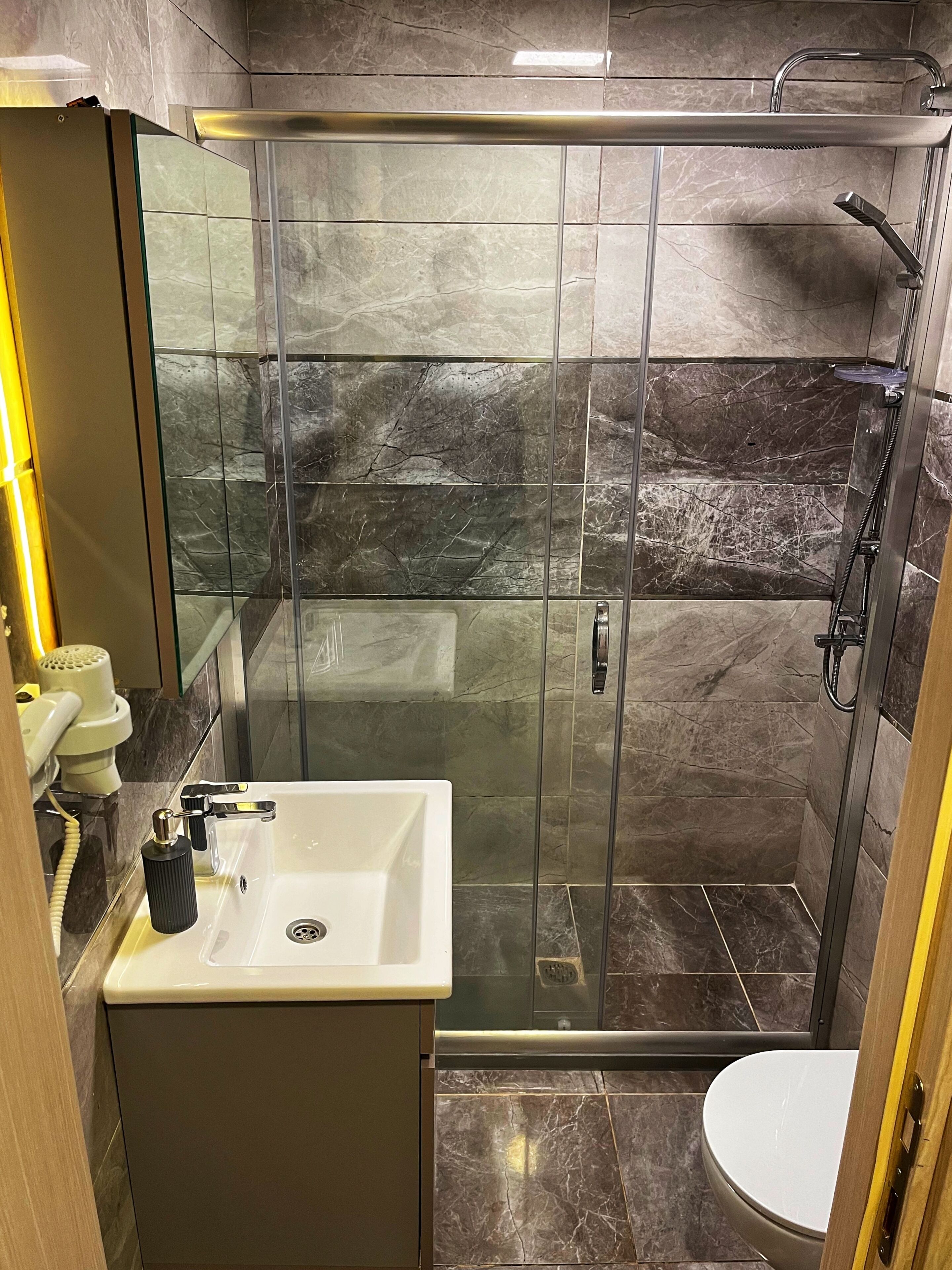 A modern bathroom with a glass-enclosed shower, a white sink, and a toilet.