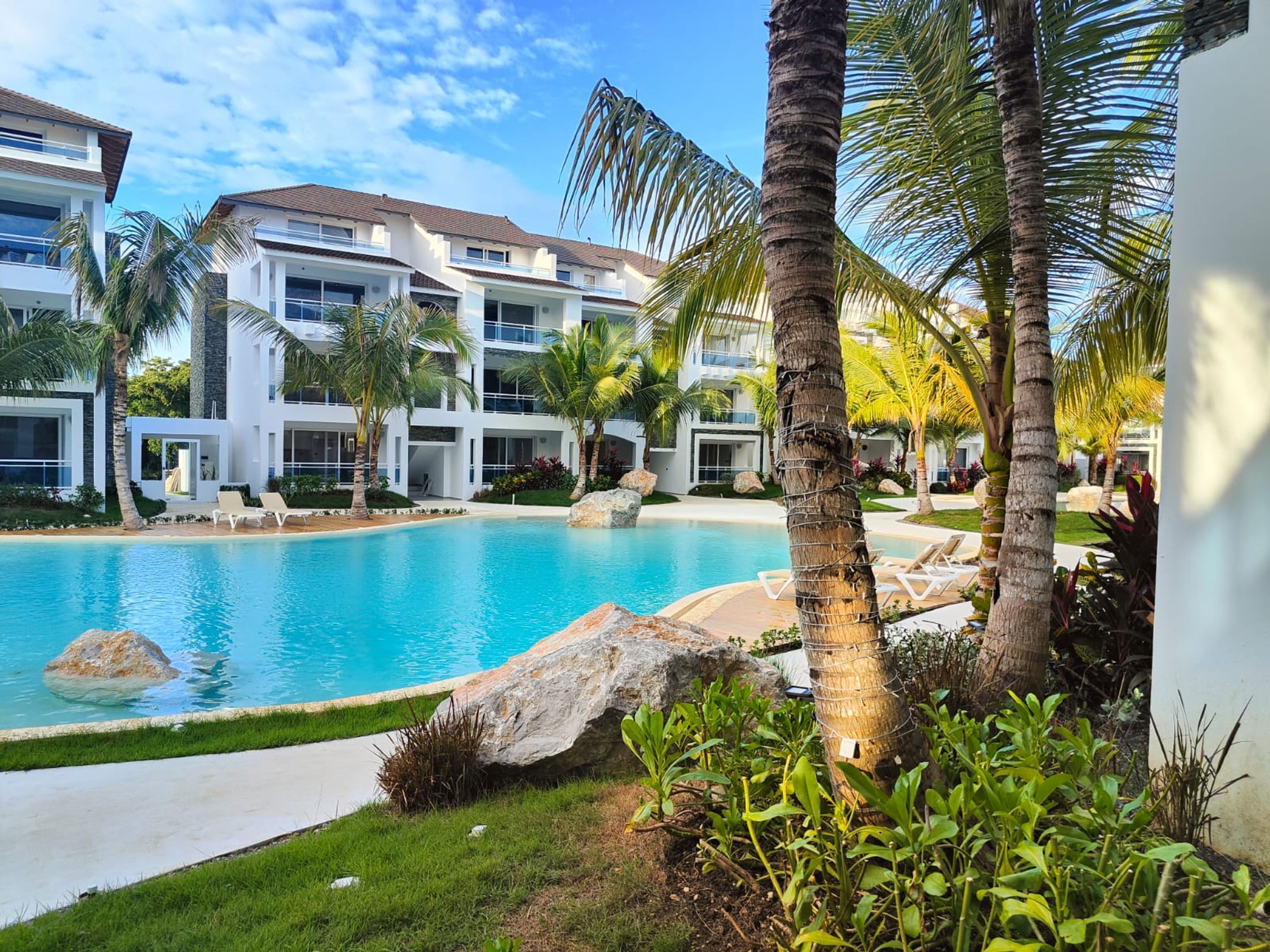 Ein modernes Hotel mit Schwimmbad, Palmen und blauem Himmel.